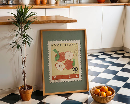 a framed Italian postage stamp with an illustration of apples and oranges, placed on a checkered floor next to a potted plant and a basket of oranges.
