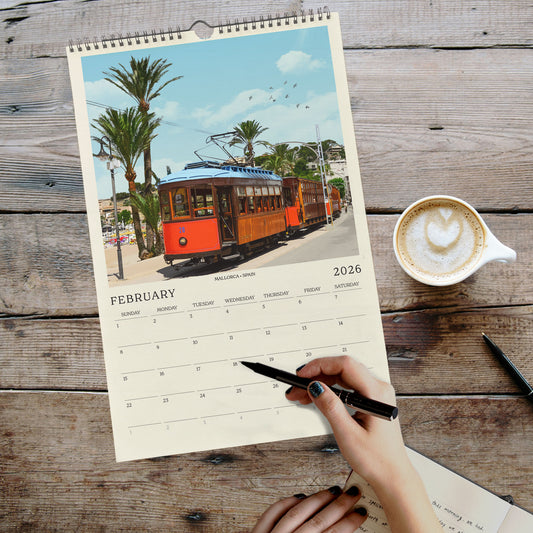 A person is writing in a notebook while holding a pen, with a calendar featuring a trolley car image on the wall behind them.