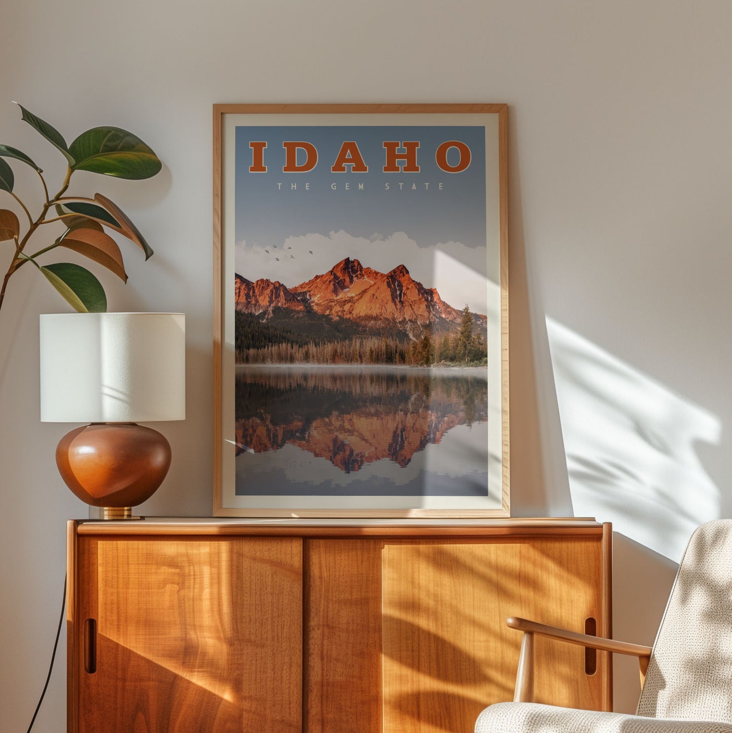 a framed poster of a mountain landscape with a lake, hanging on a wall above a wooden cabinet.