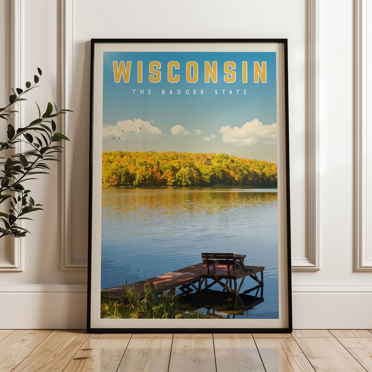 A framed poster of a scenic lake with a dock and bench, surrounded by autumn foliage, with the text "WISCONSIN THE BADGER STATE" prominently displayed.