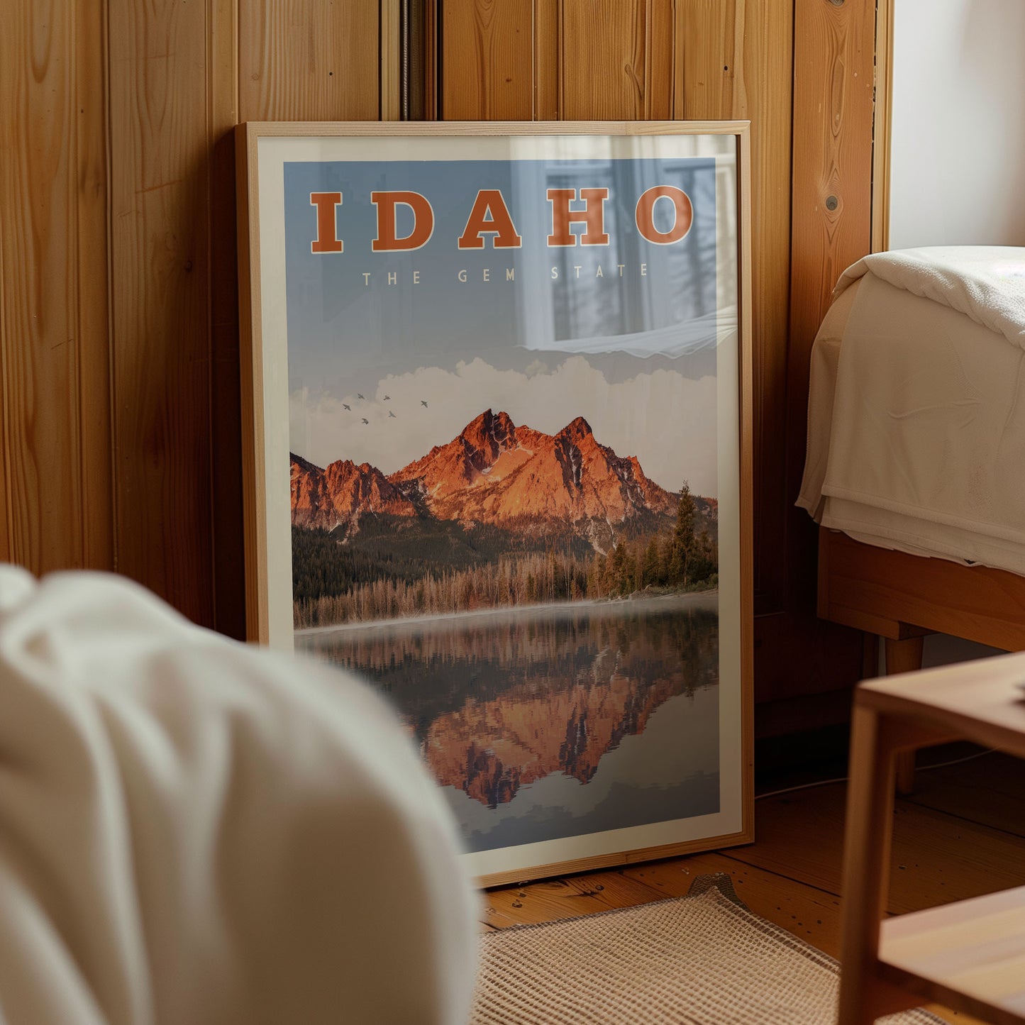 A framed poster of a mountain landscape with a lake in the foreground, displayed in a room with wooden walls.