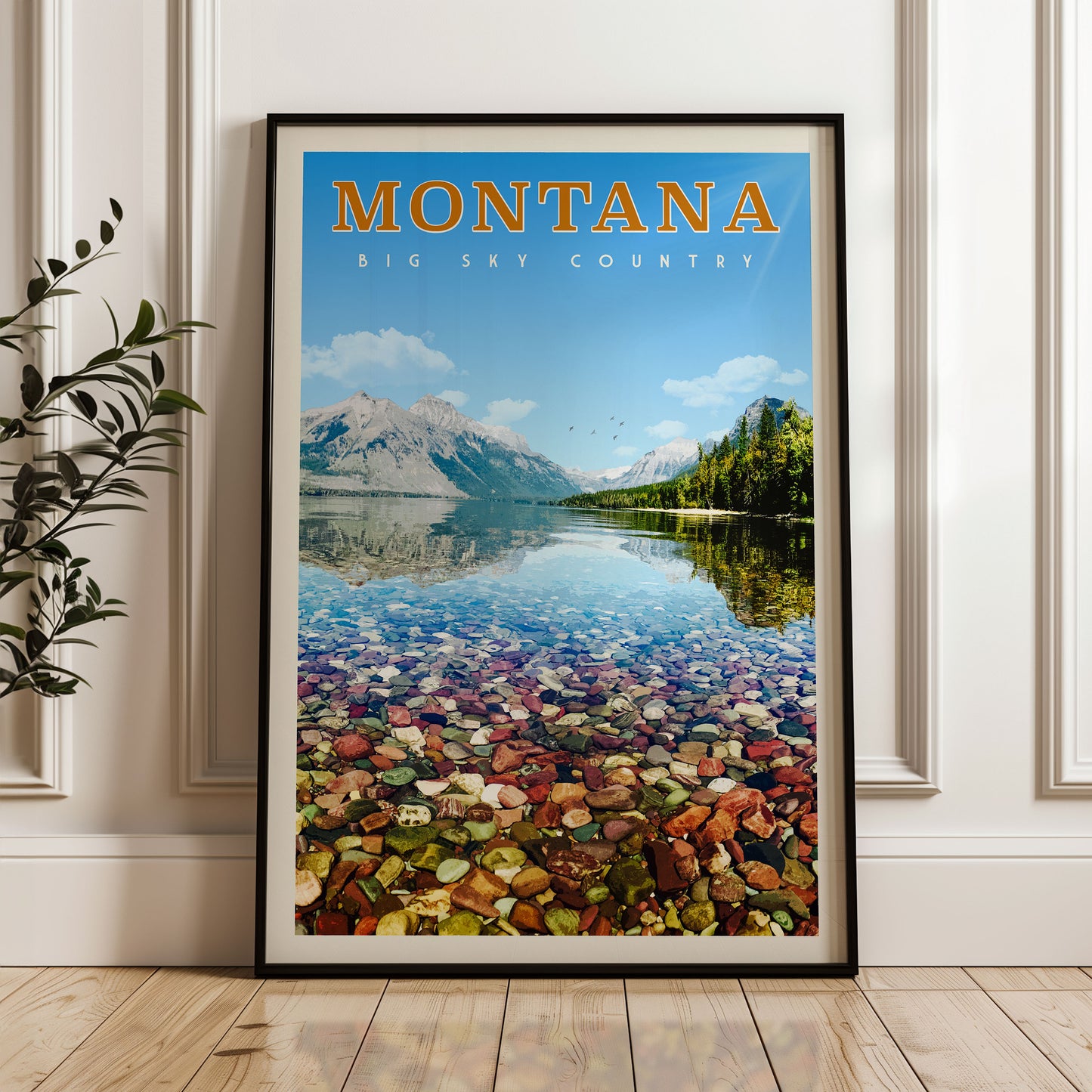A framed poster of a scenic landscape in Montana, featuring a mountain range, a lake, and a rocky shore with colorful pebbles.