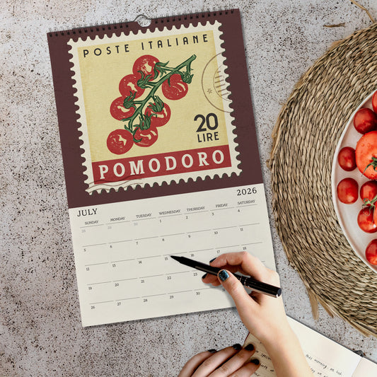 a person's hand holding a pen, writing on a calendar that has a tomato stamp design. The calendar is placed on a table, and there is a plate of tomatoes nearby.