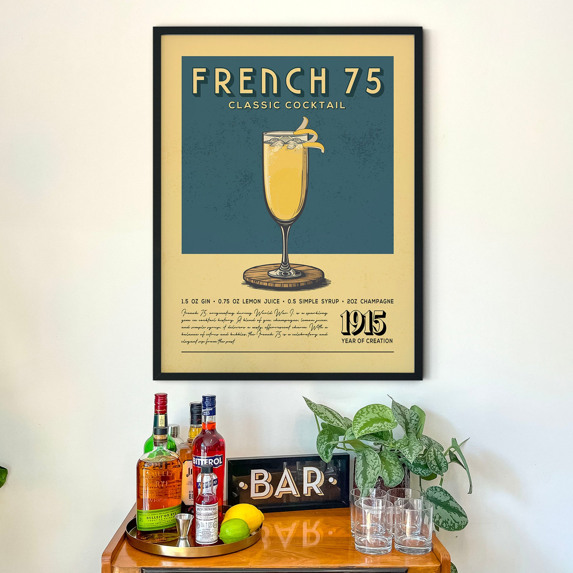 a framed poster of a French 75 cocktail hanging on a wall above a wooden bar counter with various liquor bottles and glasses.