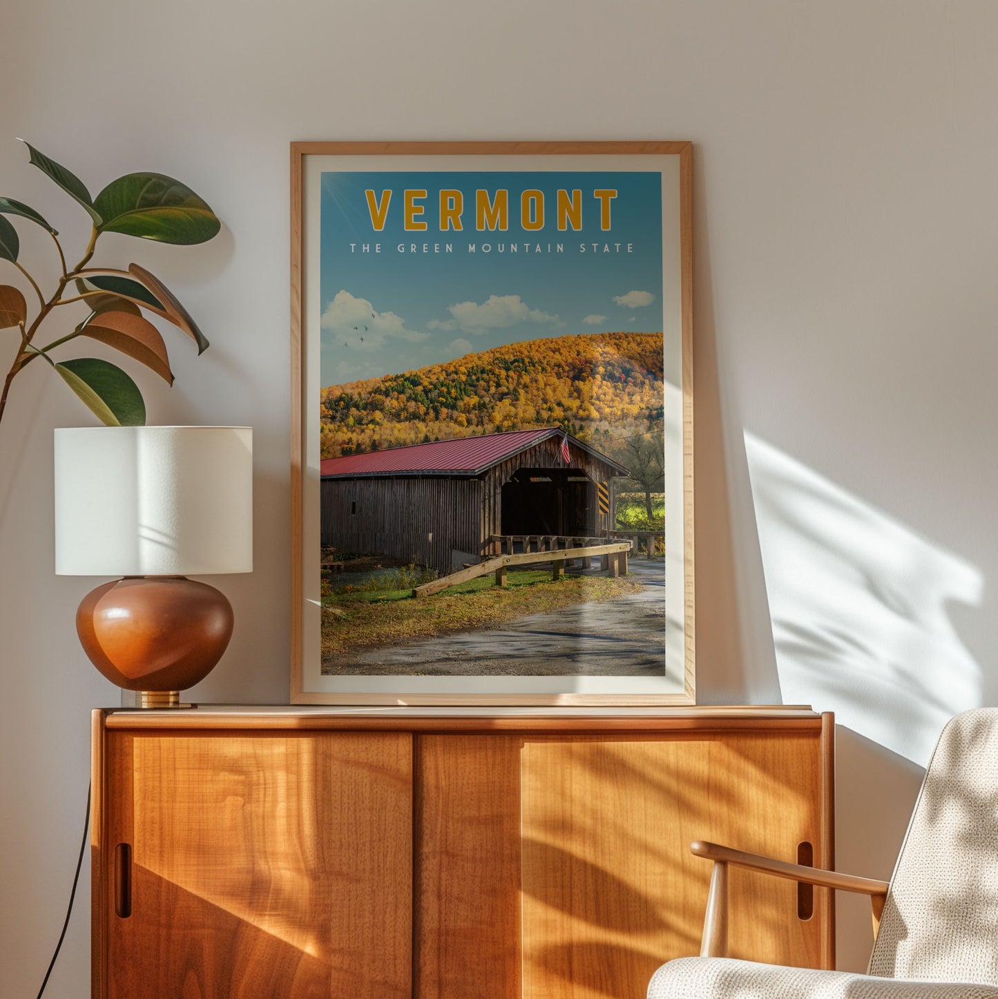 a framed poster of a wooden cabin with a red roof, set against a backdrop of a mountain and trees, hanging on a wall.