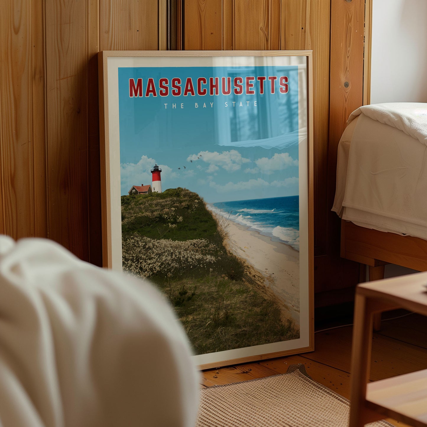 A framed poster of a lighthouse on a beach in Massachusetts, with the text "MASSACHUSETTS THE BAY STATE" prominently displayed.