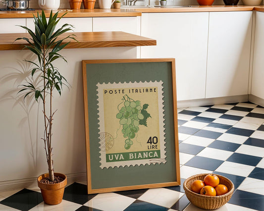 a framed Italian postage stamp with a green border and a white background, placed on a checkered floor next to a potted plant and a basket of oranges.