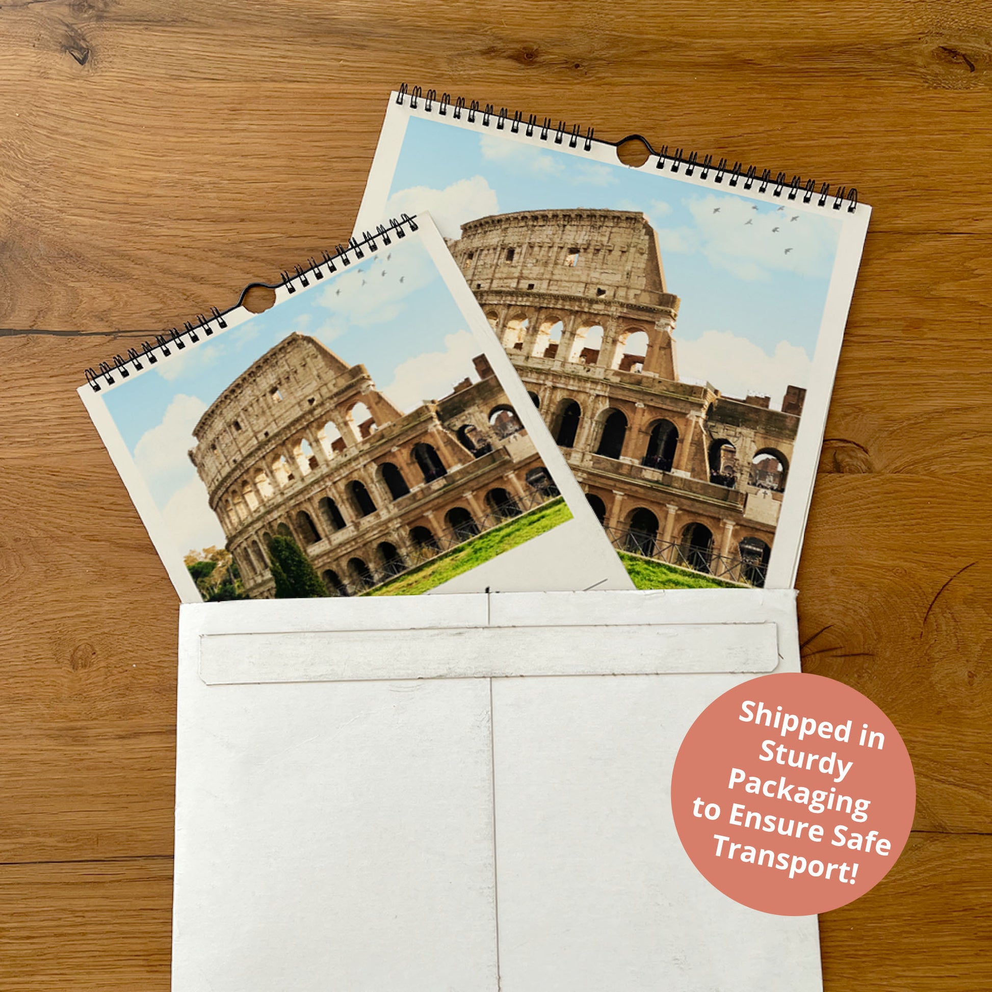 a spiral-bound calendar with a photograph of the Colosseum, a famous landmark in Rome, Italy. The calendar is placed inside a white envelope, and there is a red circular sticker on the envelope that reads "Shipped in Sturdy Packaging to Ensure Safe Transport!"