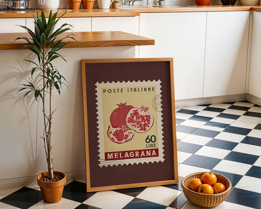 a framed Italian postage stamp with a pomegranate design, placed on a checkered floor next to a potted plant and a basket of oranges.