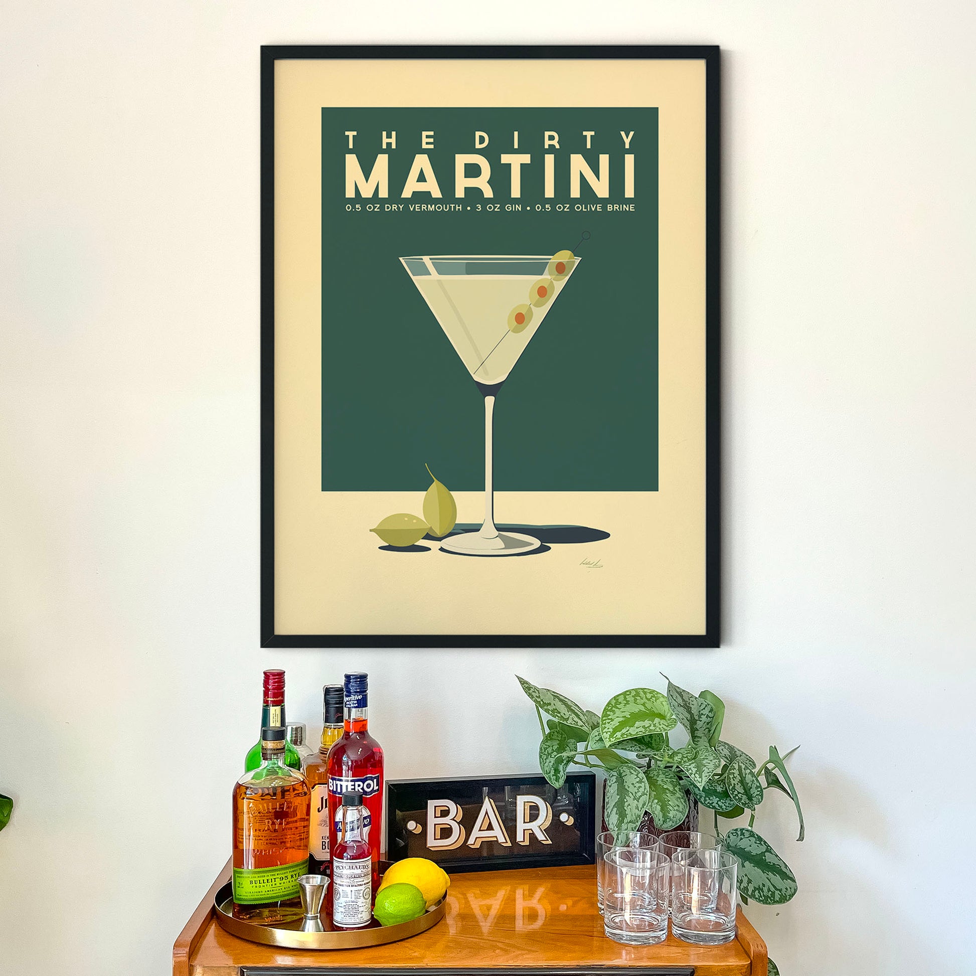 a framed poster of a martini glass with a cocktail, accompanied by a wooden bar display with various liquor bottles and glasses.