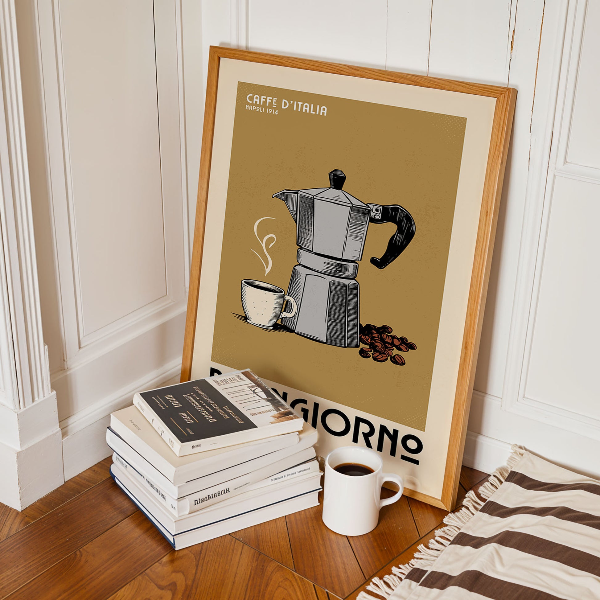 A framed poster of a coffee maker is leaning against a wall, with a stack of books and a cup of coffee nearby.