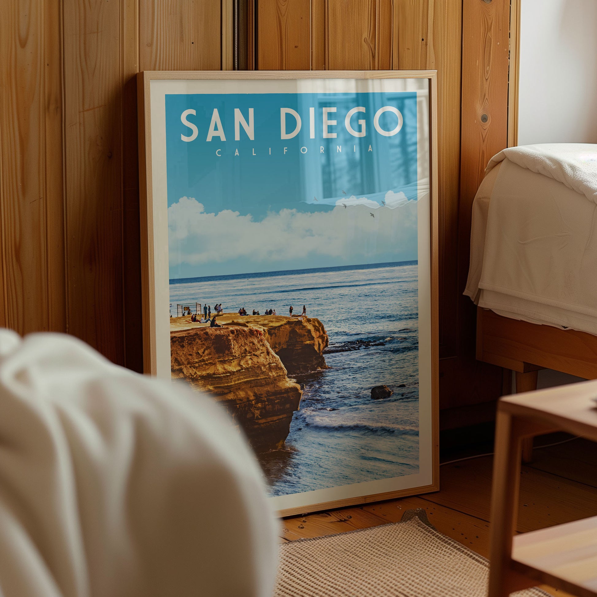 A framed poster of a scenic coastal landscape with cliffs and people enjoying the view, displayed in a room with wooden walls.