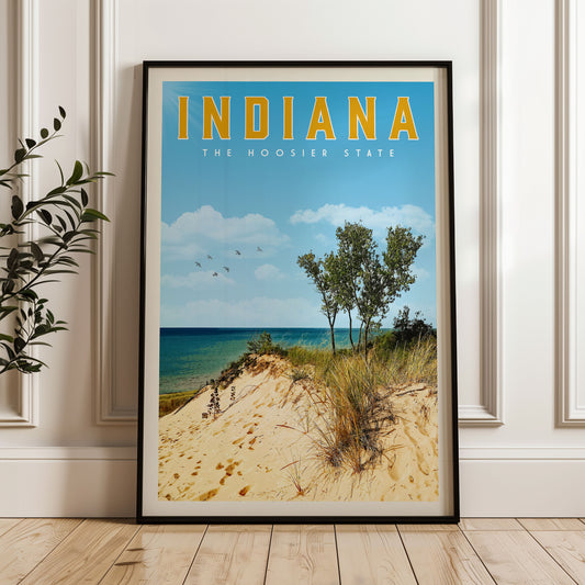 A framed poster of a beach scene with sand dunes, trees, and a body of water, with the text "INDIANA THE HOOSIER STATE" prominently displayed.
