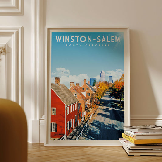 A framed poster of Winston-Salem, North Carolina, featuring a street scene with red houses and a blue sky.