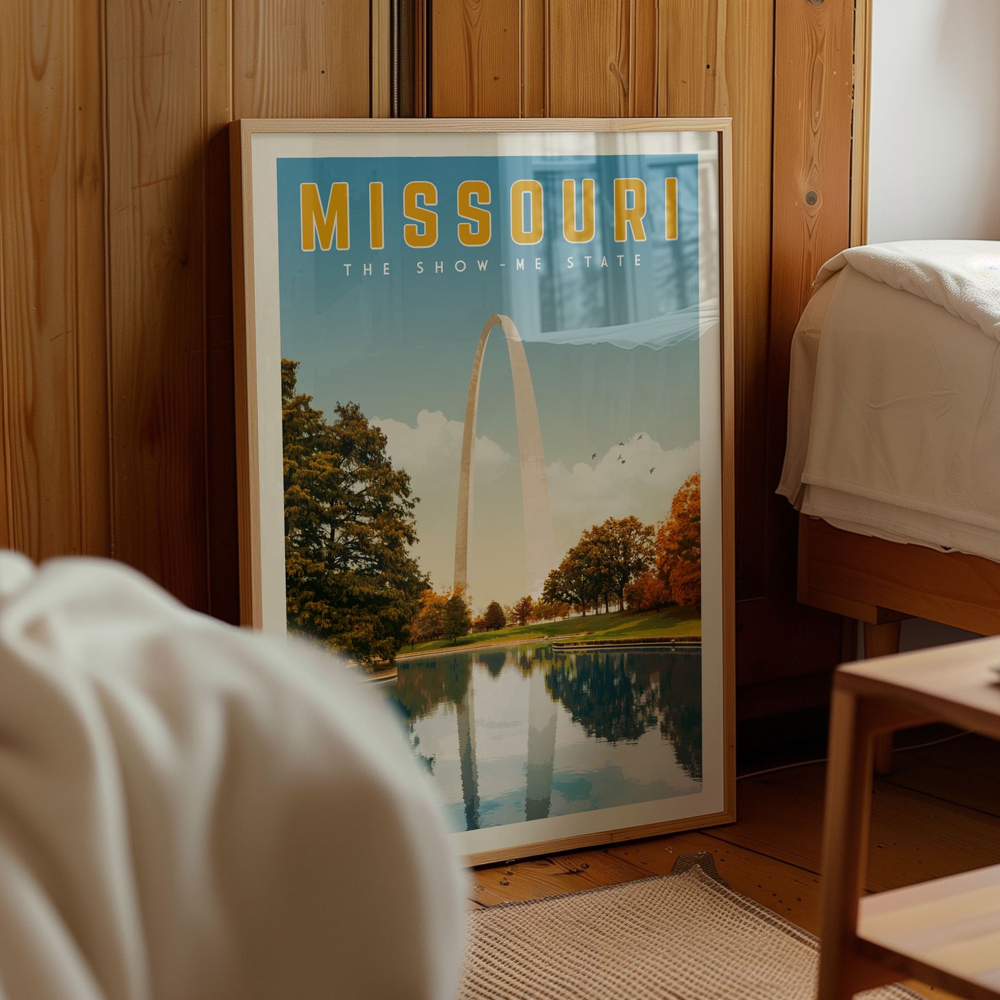 A framed poster of the Gateway Arch in Missouri, with a scenic landscape featuring the arch and trees reflected in a body of water.