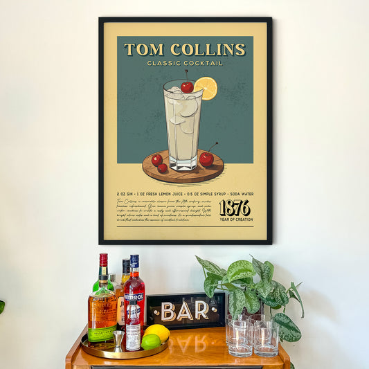 a framed poster of a classic cocktail called "Tom Collins" hanging on a wall above a wooden bar counter.