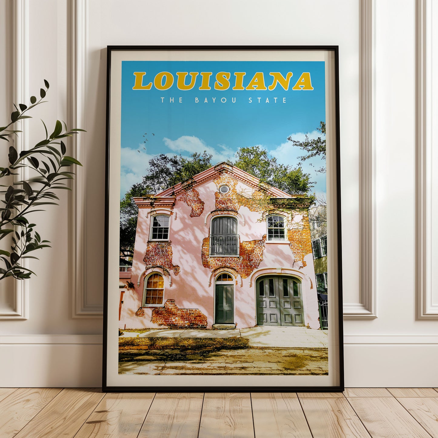 A framed poster of a pink building with a green door and windows, set against a blue sky with trees, in the state of Louisiana.