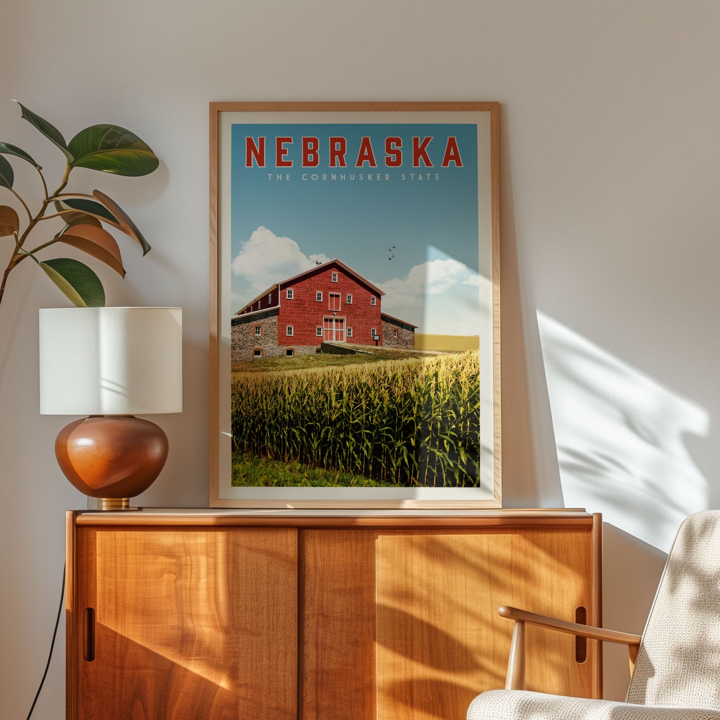 a framed poster of a red barn with a cornfield in the background, hanging on a wall next to a wooden cabinet and a lamp.