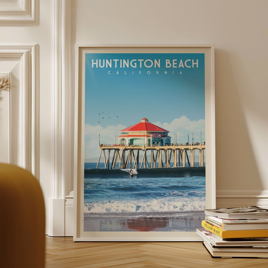 A framed poster of Huntington Beach, California, featuring a red-roofed pier and a surfer riding a wave.