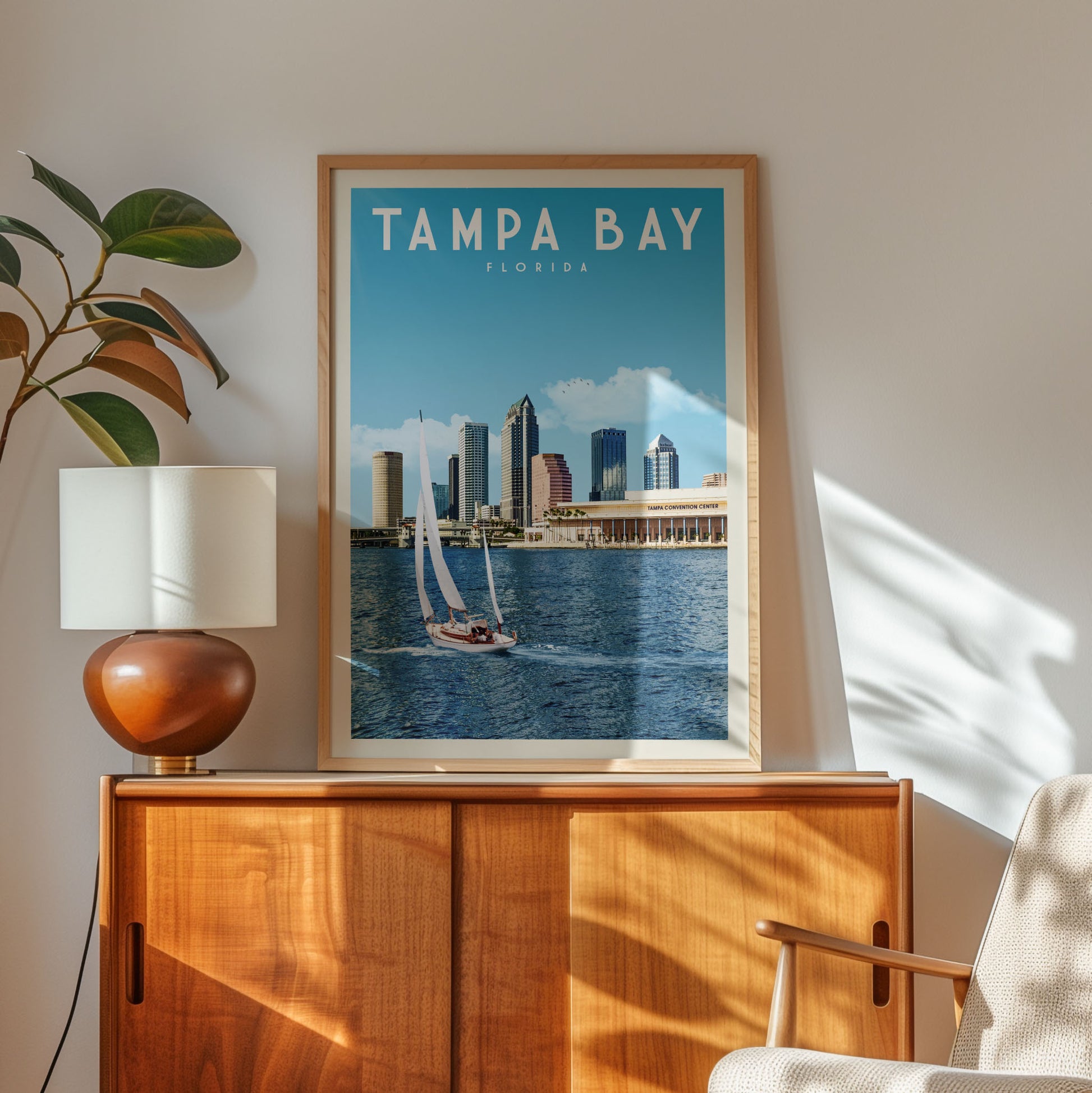 a framed poster of Tampa Bay, Florida, with a sailboat on the water, placed on a wooden cabinet or dresser.