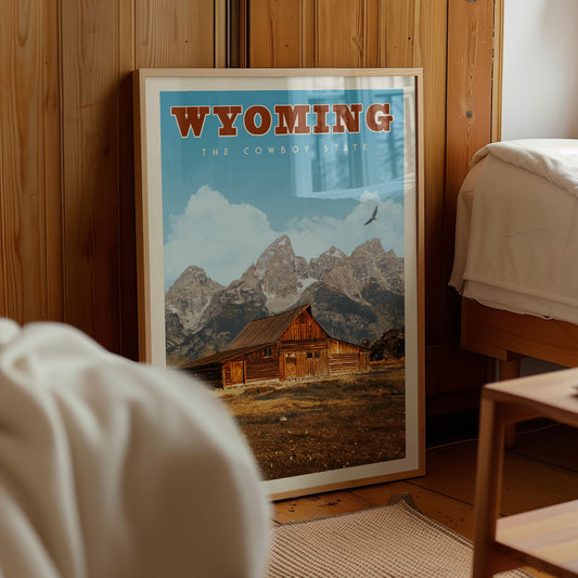 A framed poster of a cabin in the mountains, with the text "Wyoming" prominently displayed, is the central focus of the image.