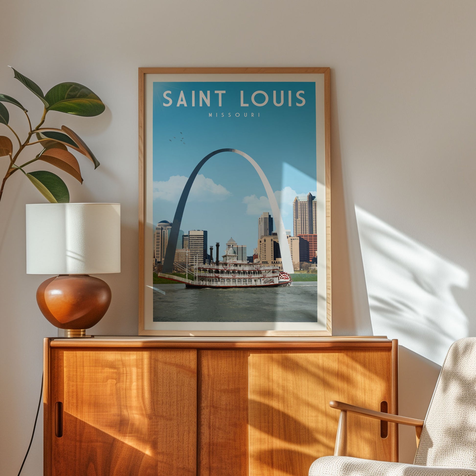 a framed poster of the Gateway Arch in St. Louis, Missouri, with a wooden cabinet below it and a plant to the left.