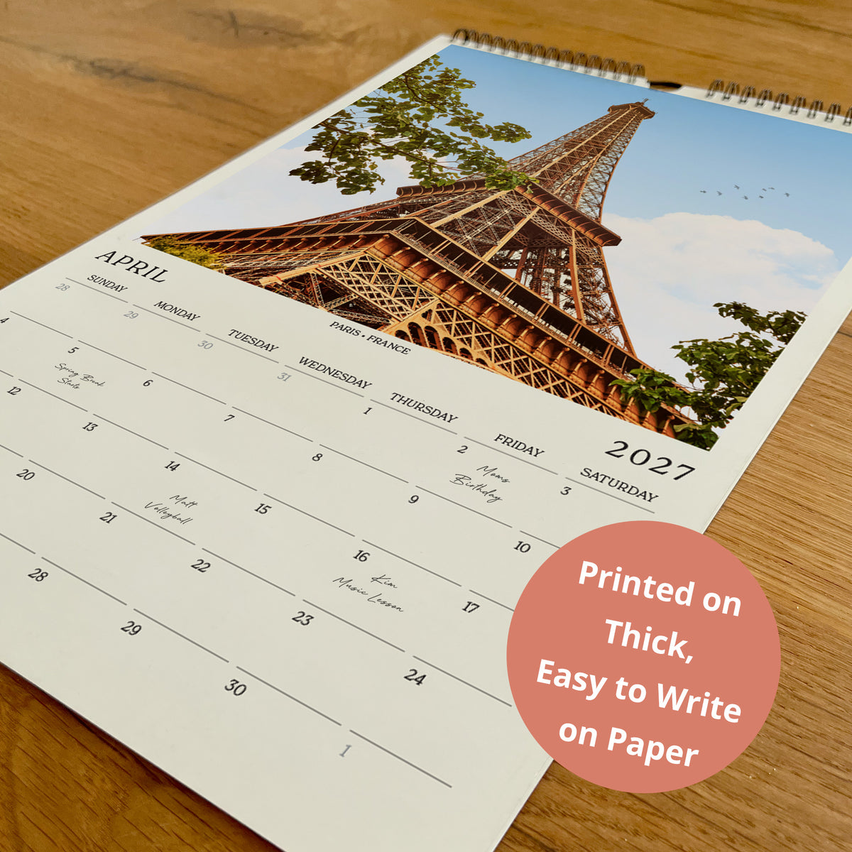 A wall calendar with a photo of the Eiffel Tower on the cover, and the text "Printed on Thick, Easy to Write on Paper" in the bottom right corner.