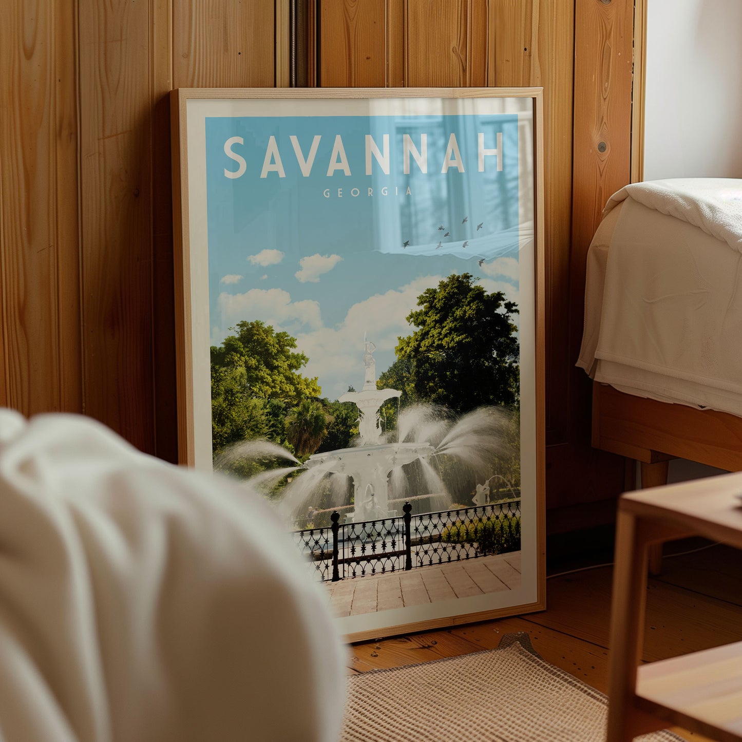 A framed poster of a fountain in Savannah, Georgia, displayed in a room with wooden paneling.