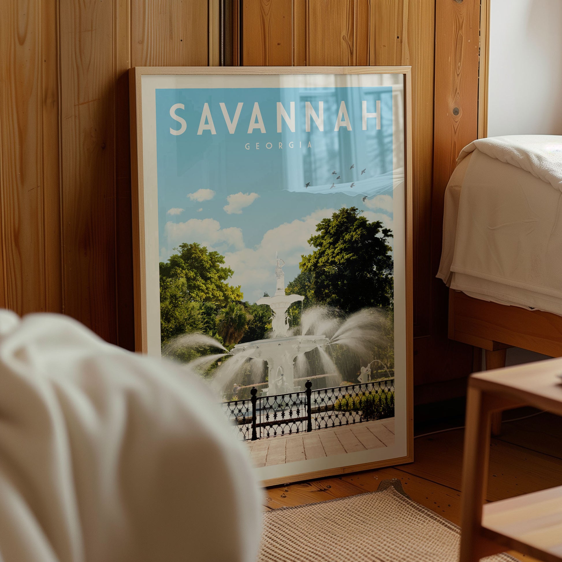 A framed poster of a fountain in Savannah, Georgia, displayed in a room with wooden paneling.