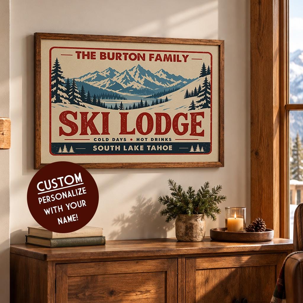 a framed poster of a mountain landscape with a ski lodge, along with a potted plant and some candles on a wooden cabinet.