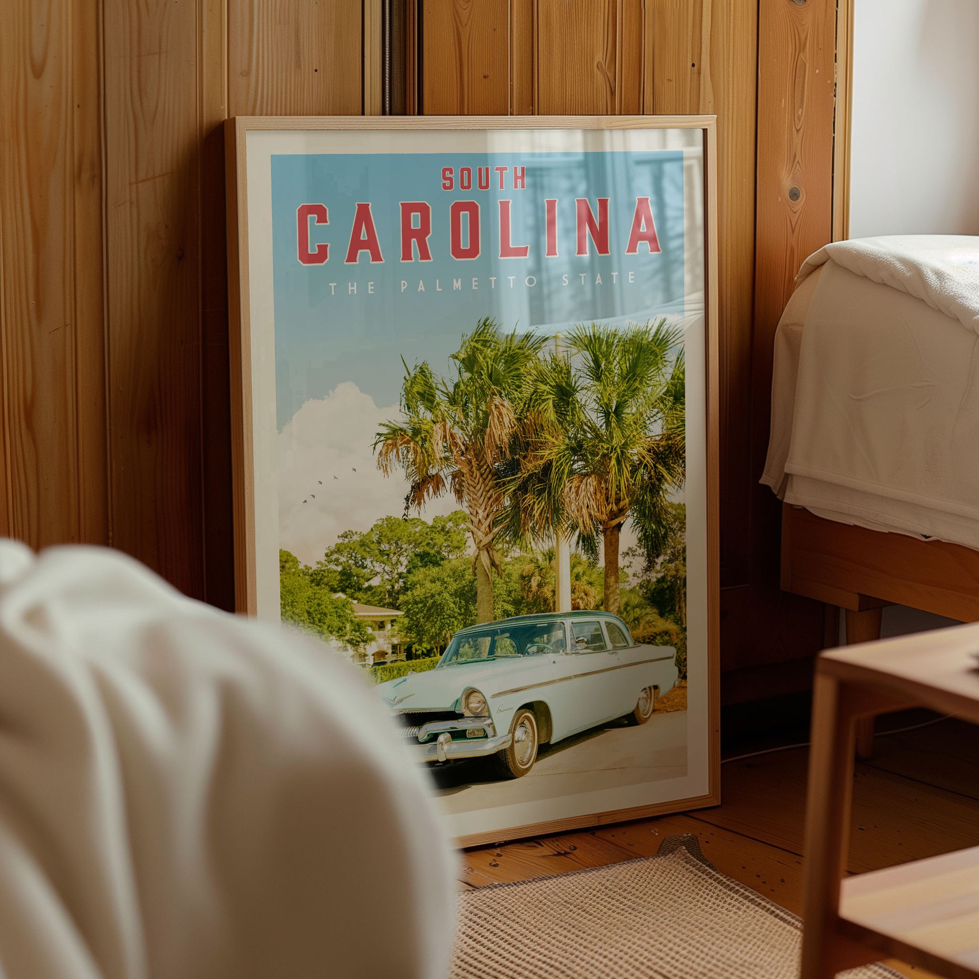 A framed poster of a car in a tropical setting, with palm trees and a house in the background, is displayed in a room with wooden walls.