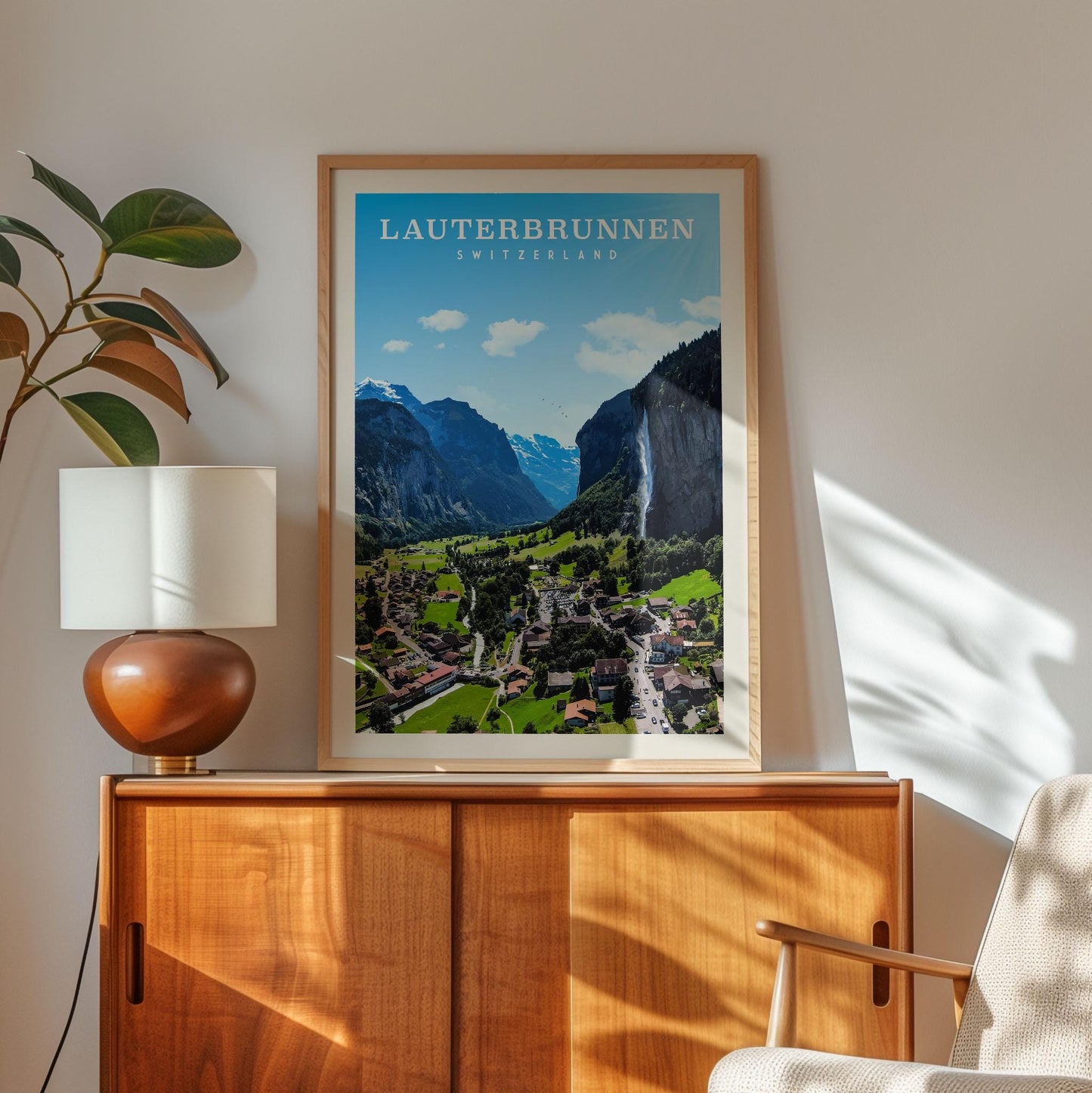 a framed poster of a scenic mountain landscape in Switzerland, with a wooden cabinet and a lamp in the foreground.