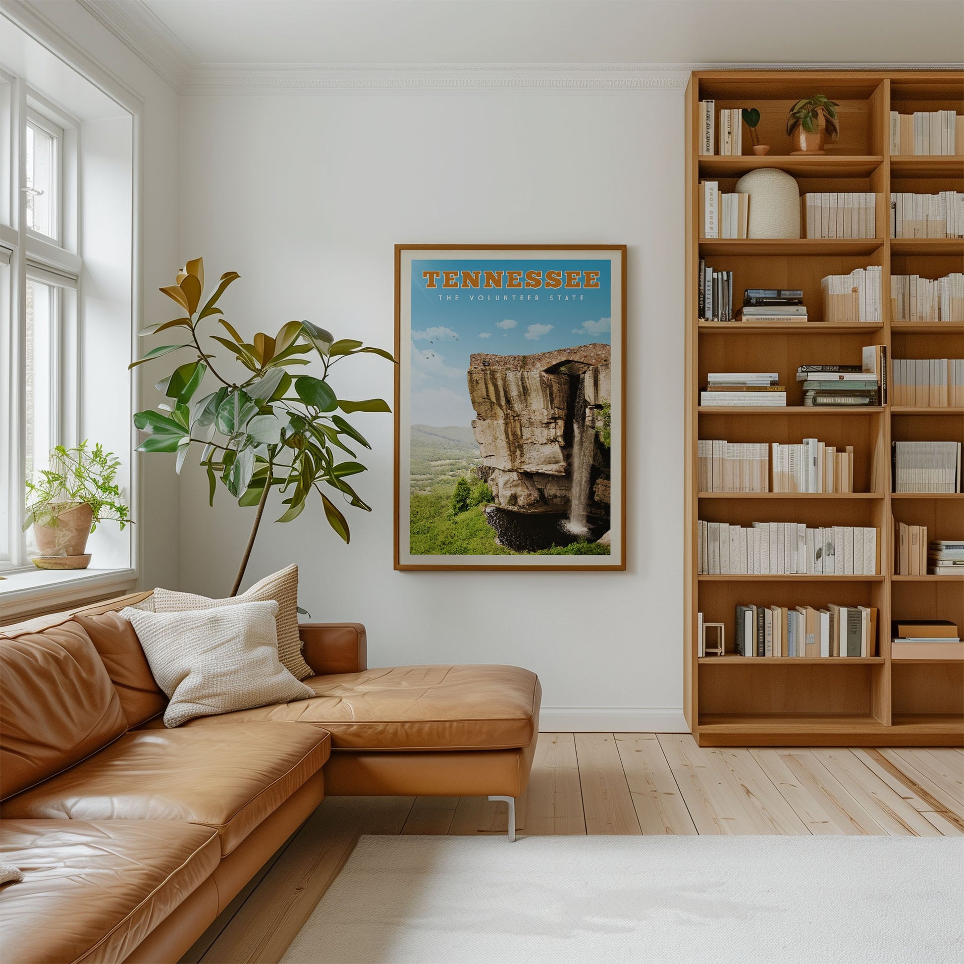a cozy living room with a large window, a comfortable leather couch, a bookshelf filled with books, and a framed poster of a scenic landscape hanging on the wall.
