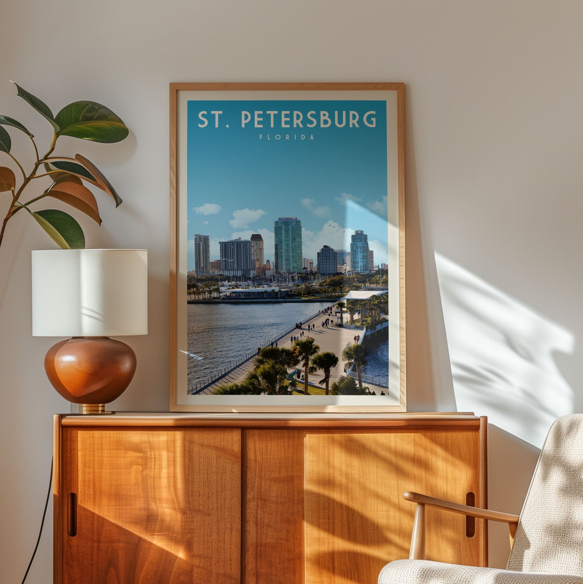 a framed poster of St. Petersburg, Florida, with a cityscape and a body of water visible, hanging on a wall above a wooden cabinet.