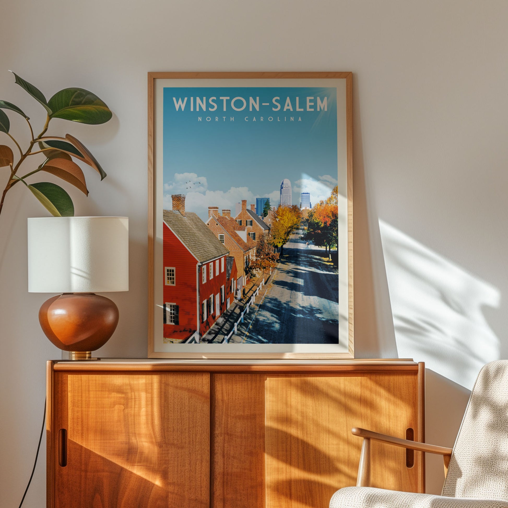a framed poster of Winston-Salem, North Carolina, with a view of the city's streets and buildings, placed on a wooden cabinet or shelf.