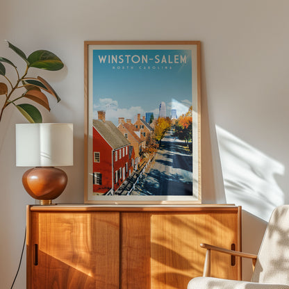 a framed poster of Winston-Salem, North Carolina, with a view of the city's streets and buildings, placed on a wooden cabinet or shelf.