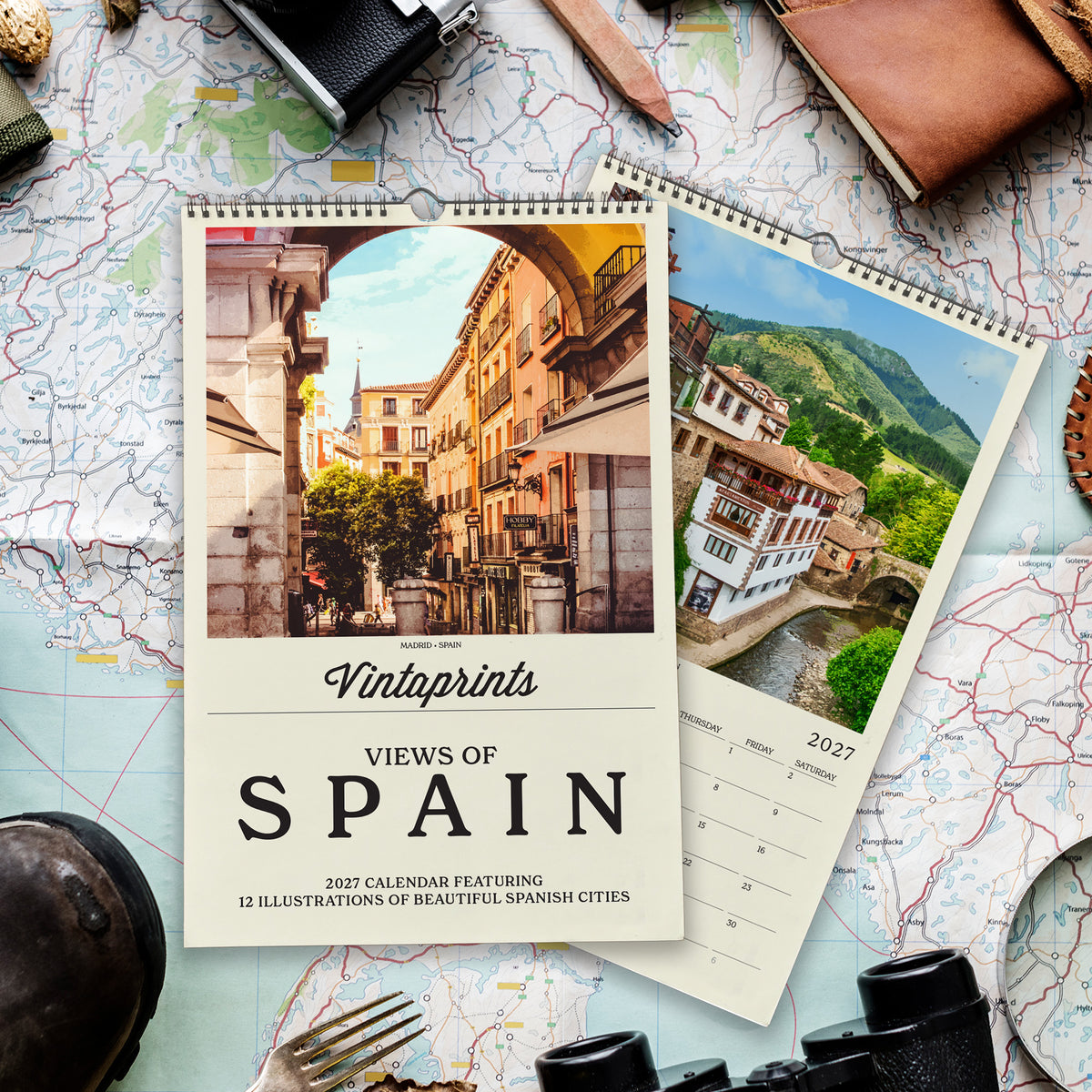 a calendar with a photo of a city in Spain, surrounded by various travel-related items such as a map, a camera, and a pair of binoculars.