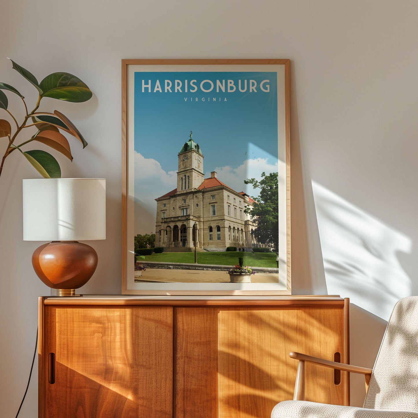 a framed poster of a historic building, specifically the Harrisonburg, Virginia, courthouse, with a wooden cabinet and a lamp in the foreground.