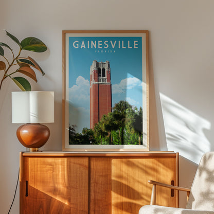 a framed poster of the Gainesville, Florida skyline, with a red brick tower and palm trees, displayed on a wooden cabinet.