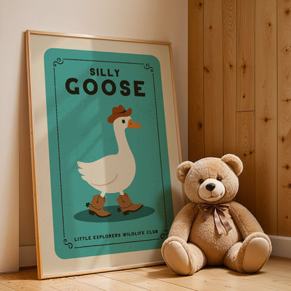 A framed poster of a cartoon goose wearing a cowboy hat and boots, with the title "Silly Goose" and the text "Little Explorers Wildlife Club" below it, is leaning against a wooden wall next to a teddy bear.