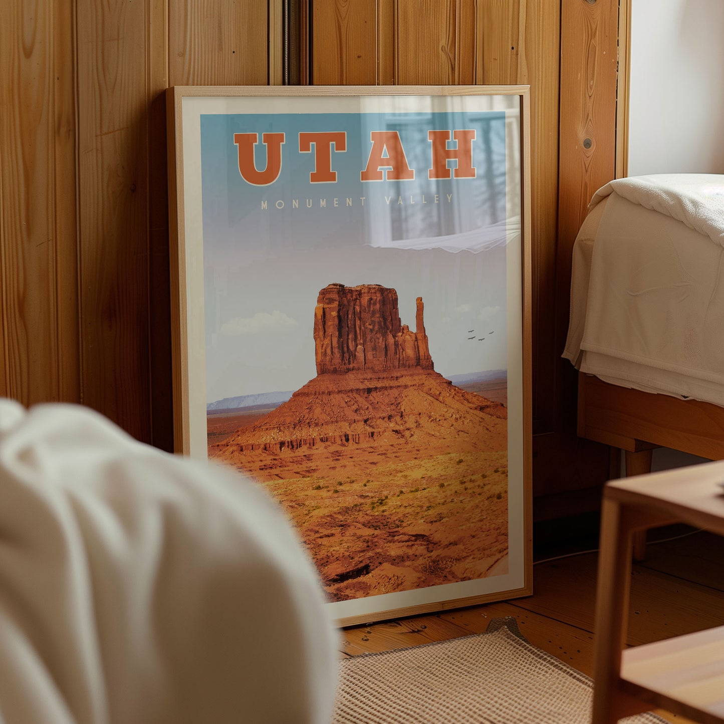 A framed poster of Monument Valley, a famous landmark in Utah, is displayed in a room with wooden walls.