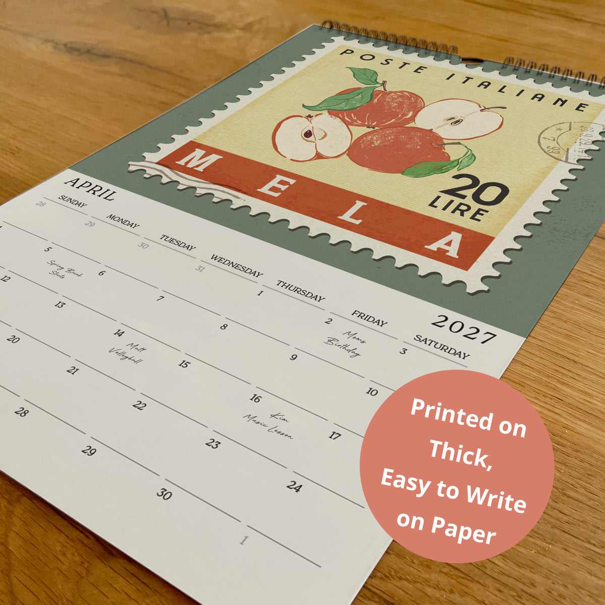 A calendar with a vintage-style stamp design on the cover, featuring an illustration of apples and a postmark. The calendar is printed on paper and placed on a wooden surface.