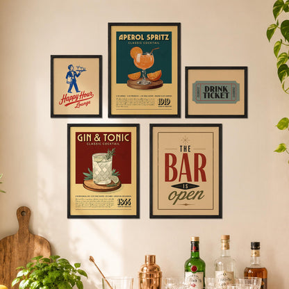 a wall with five framed vintage-style advertisements for bars and cocktails, including a poster for Aperol Spritz, a Gin & Tonic poster, and a framed ticket sign for The Bar is open. There are also several bottles of alcohol displayed on a shelf below the framed advertisements.