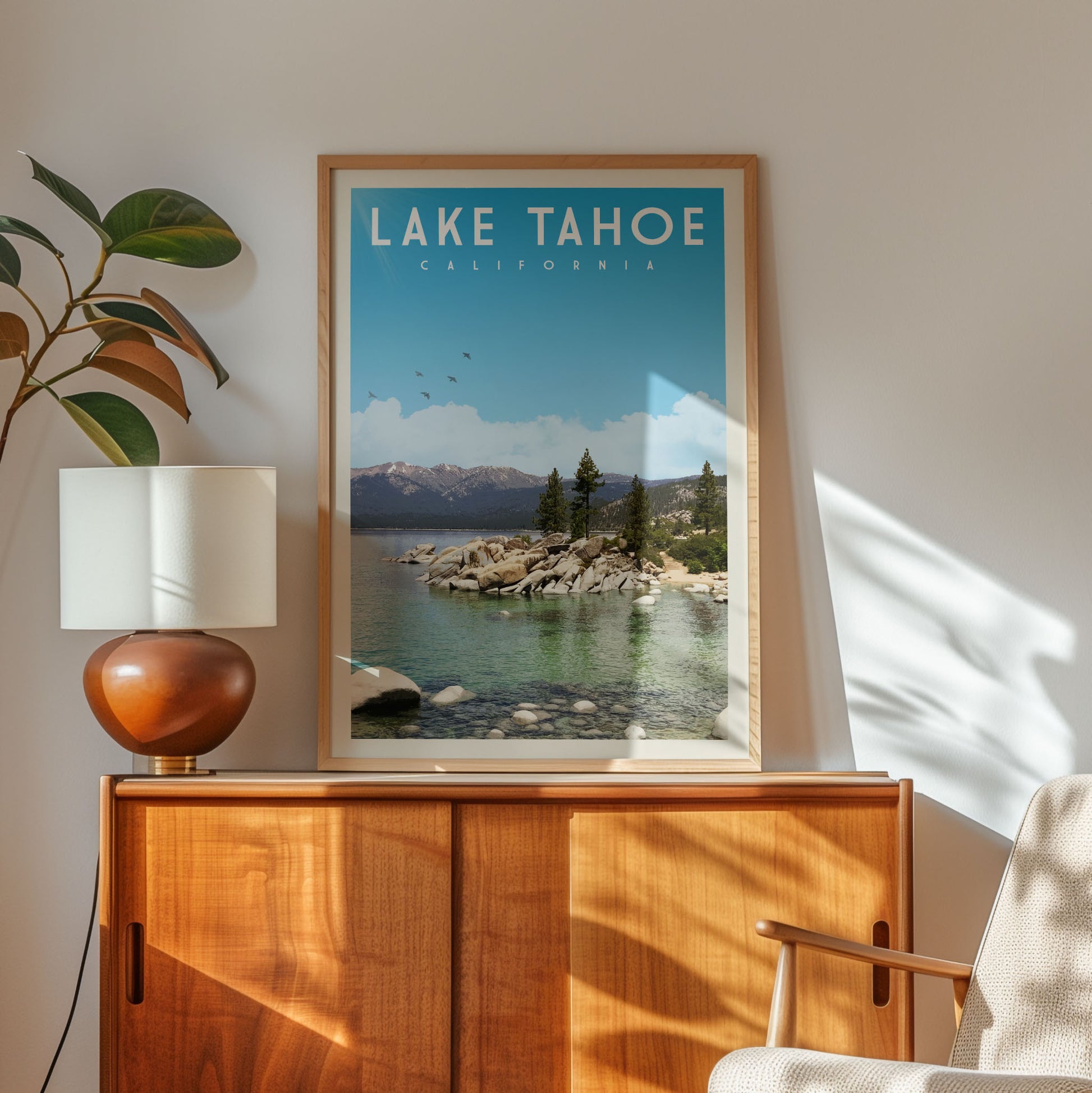 a framed poster of Lake Tahoe, California, with a scenic view of the lake and mountains in the background. The poster is displayed on a wooden cabinet, and there is a lamp and a plant nearby.