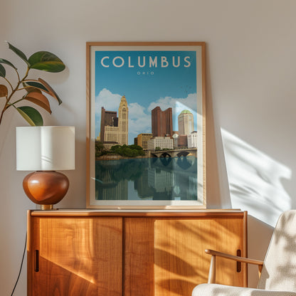 a framed poster of the Columbus, Ohio skyline, with a wooden cabinet and a lamp in the foreground.