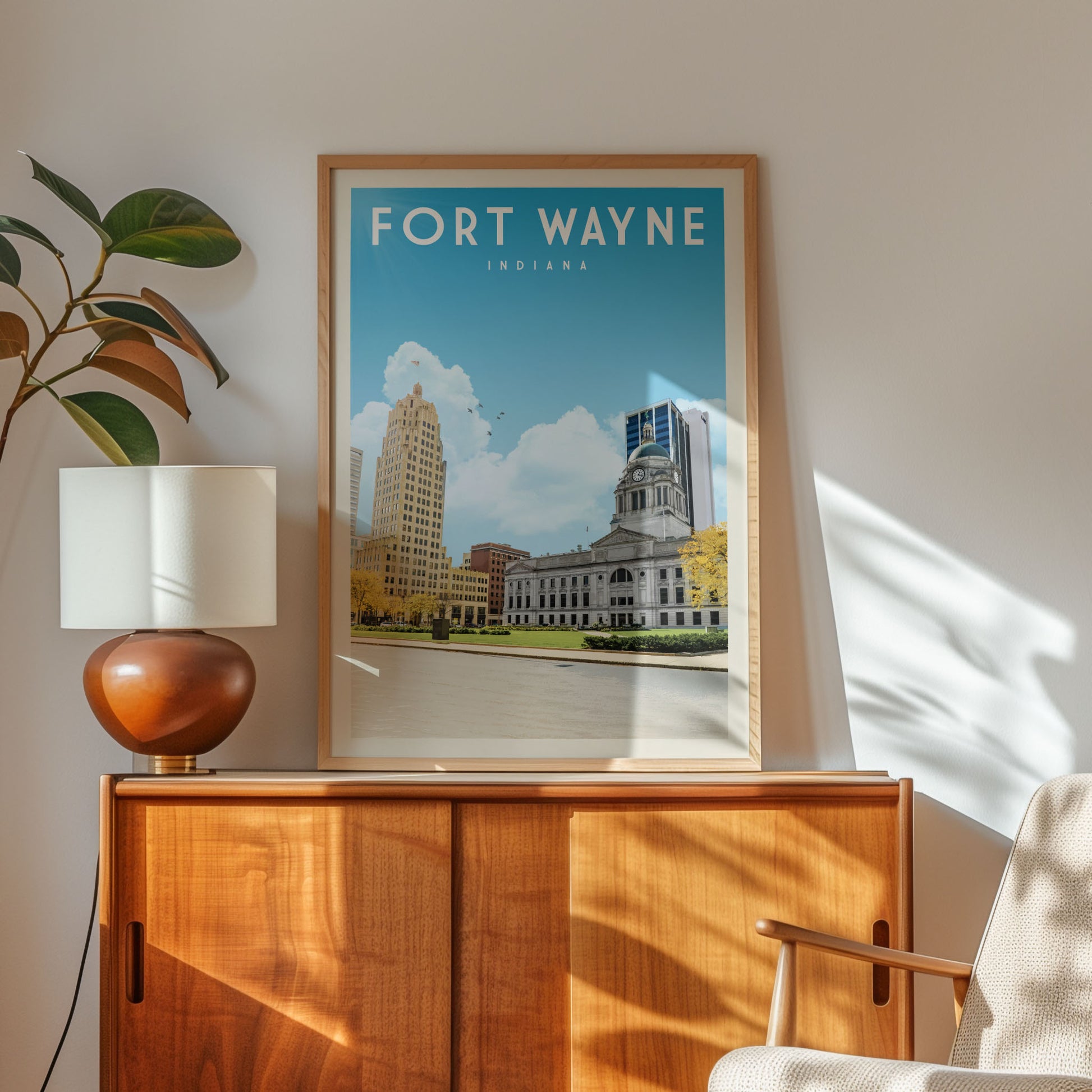 a framed poster of Fort Wayne, Indiana, with a cityscape and a building visible, placed on a wooden cabinet or shelf.