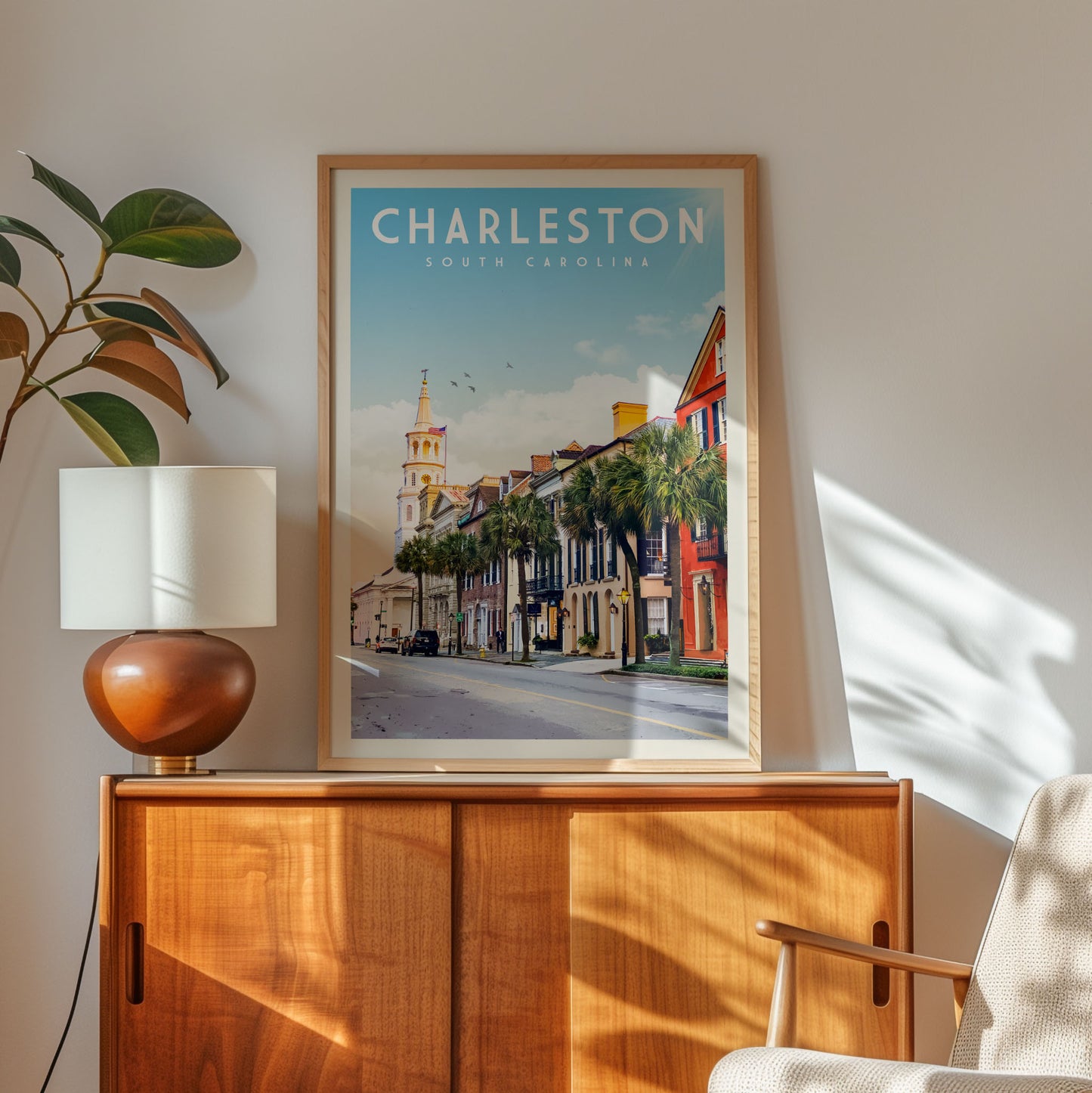 a framed poster of a street scene in Charleston, South Carolina, with a lamp and a wooden cabinet below it.