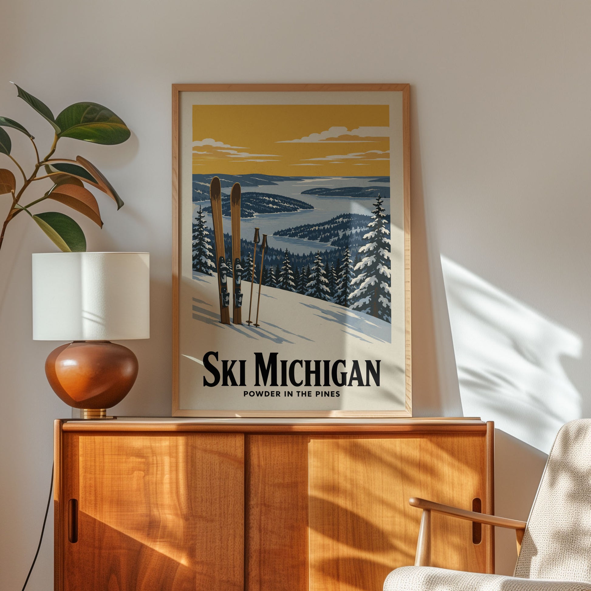 A framed poster of a snowy mountain landscape with skis and pine trees, hanging on a wall above a wooden cabinet.