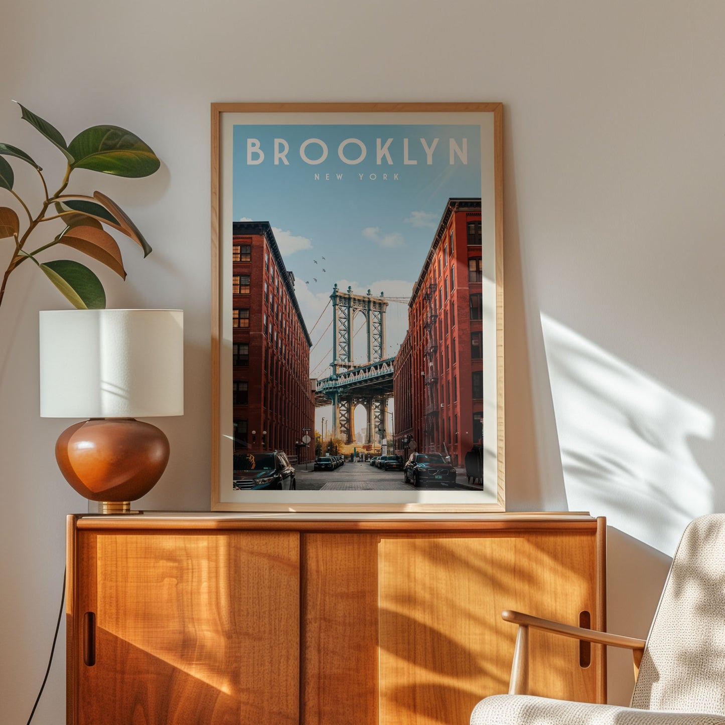 a framed poster of the Manhattan Bridge in New York City, with a wooden cabinet and a lamp in the foreground.