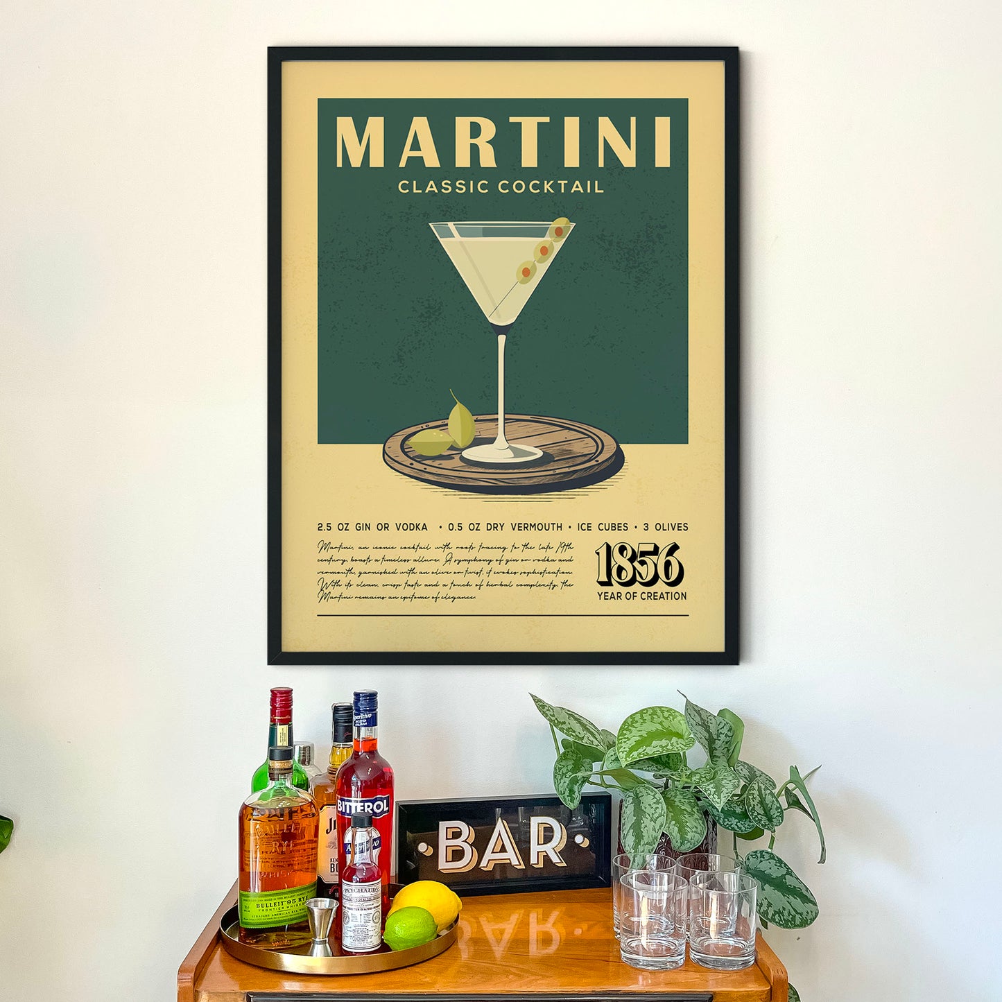 a framed poster of a martini cocktail hanging on a wall above a wooden bar counter with various liquor bottles and glasses.